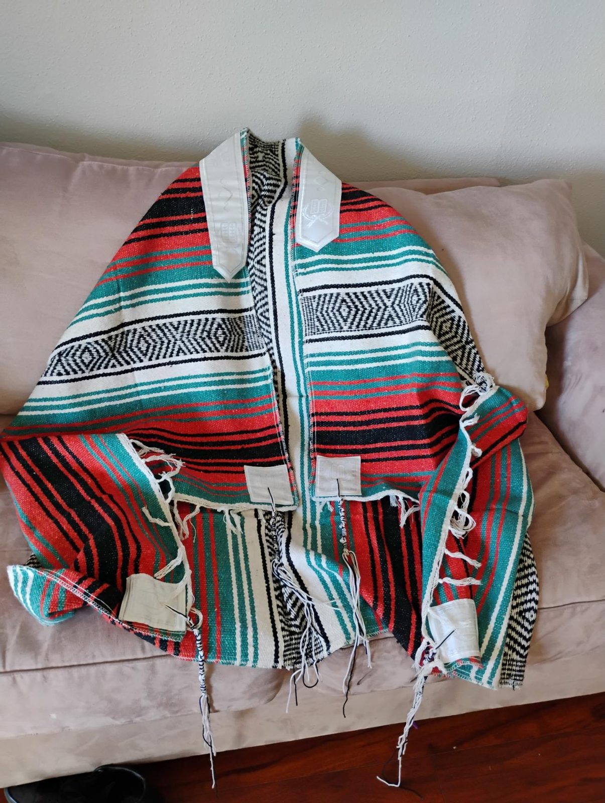 Tallit sarape Turquesa extendido en un sofá: rayas verde, rojo, negro y blanco, atará blanca, placas en las esquinas y tzitzit.